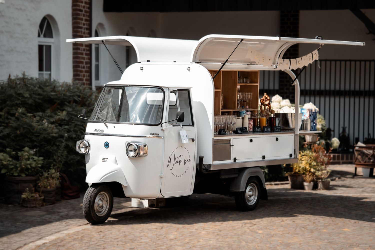White vintage Piaggio Ape three-wheeler food truck serving as a mobile bar at an outdoor event.
