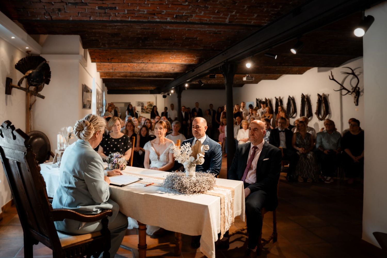 Couple signing marriage documents at a rustic wedding ceremony with guests seated in the background.