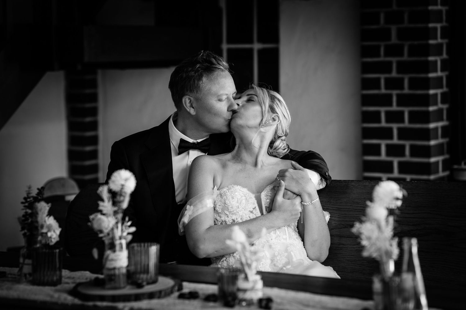 Bride and groom sharing a romantic kiss at the reception table in black and white.