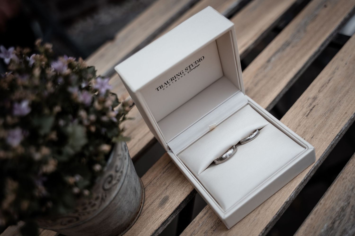 Two elegant silver wedding rings displayed in a white jewelry box on a wooden surface.