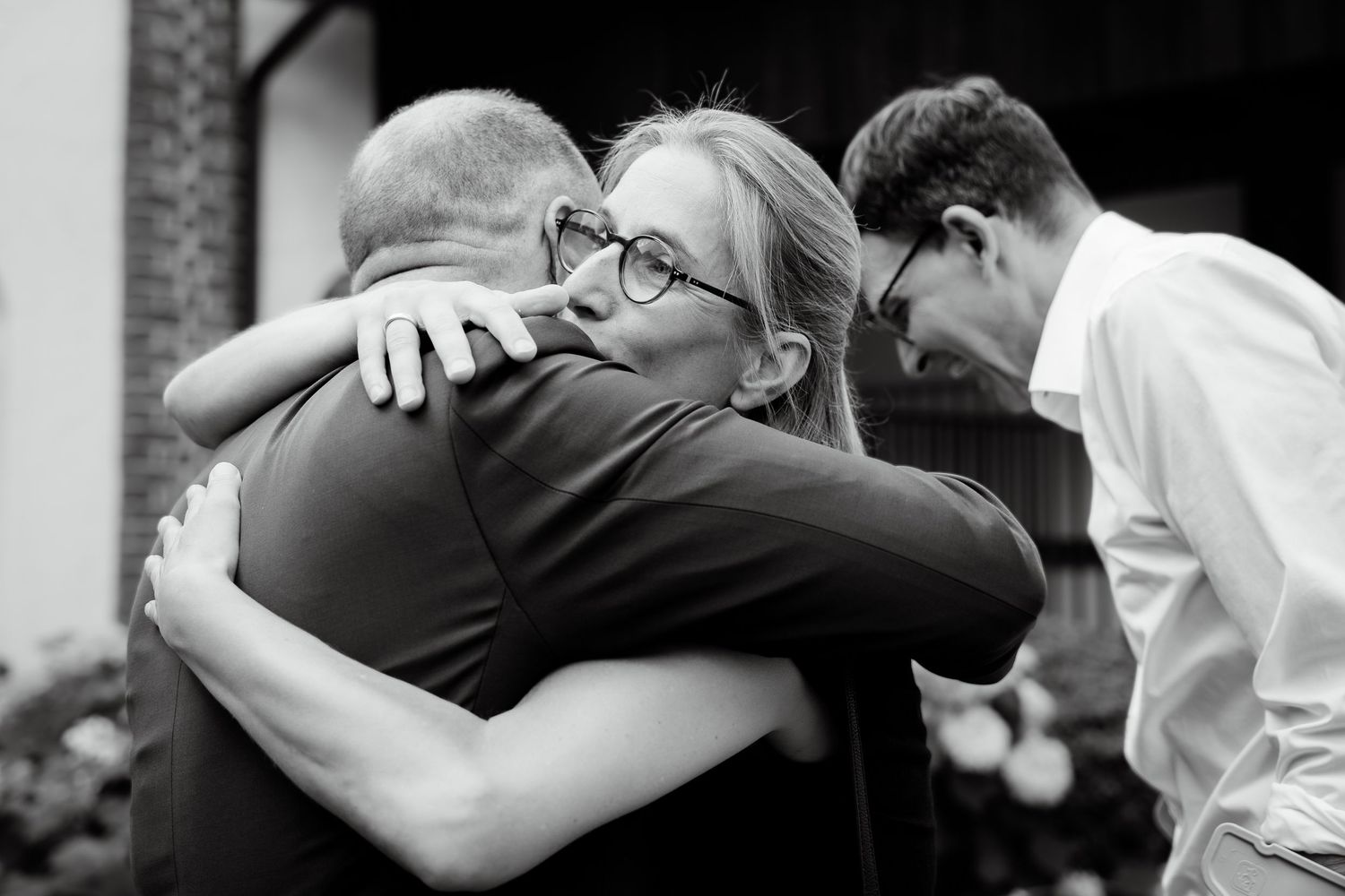 Emotional black and white photo of wedding guests embracing and hugging outside after ceremony.