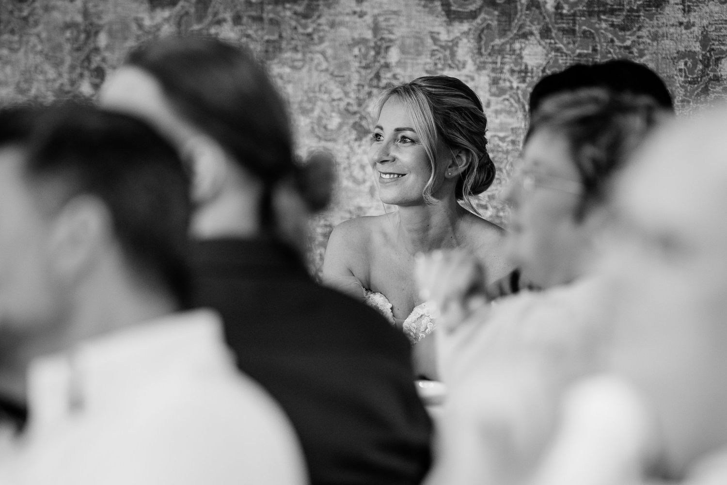 Bride smiling joyfully at wedding reception guests in elegant black and white photo.