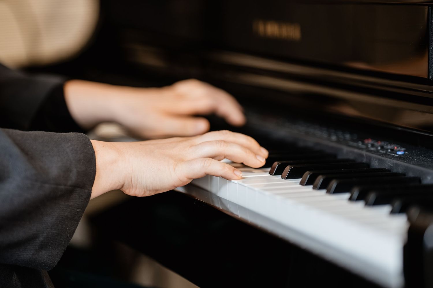 Close-up of hands playing an upright piano, fingers pressing black and white keys.