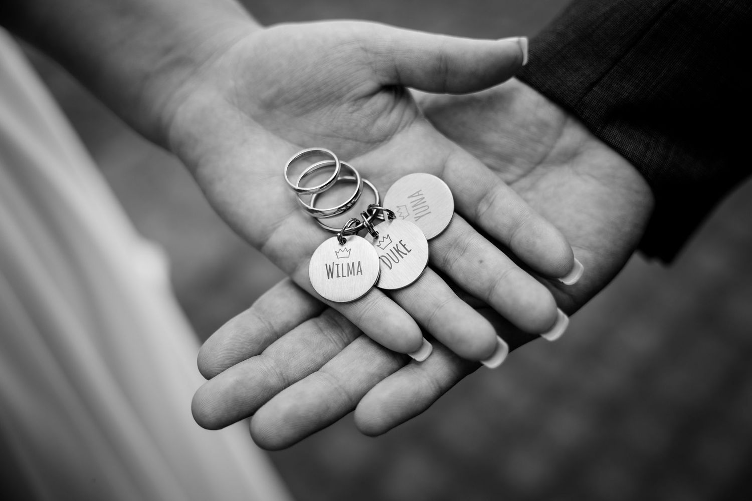 Black and white photo of two hands holding wedding rings and personalized keychains reading Wilma and Jake.
