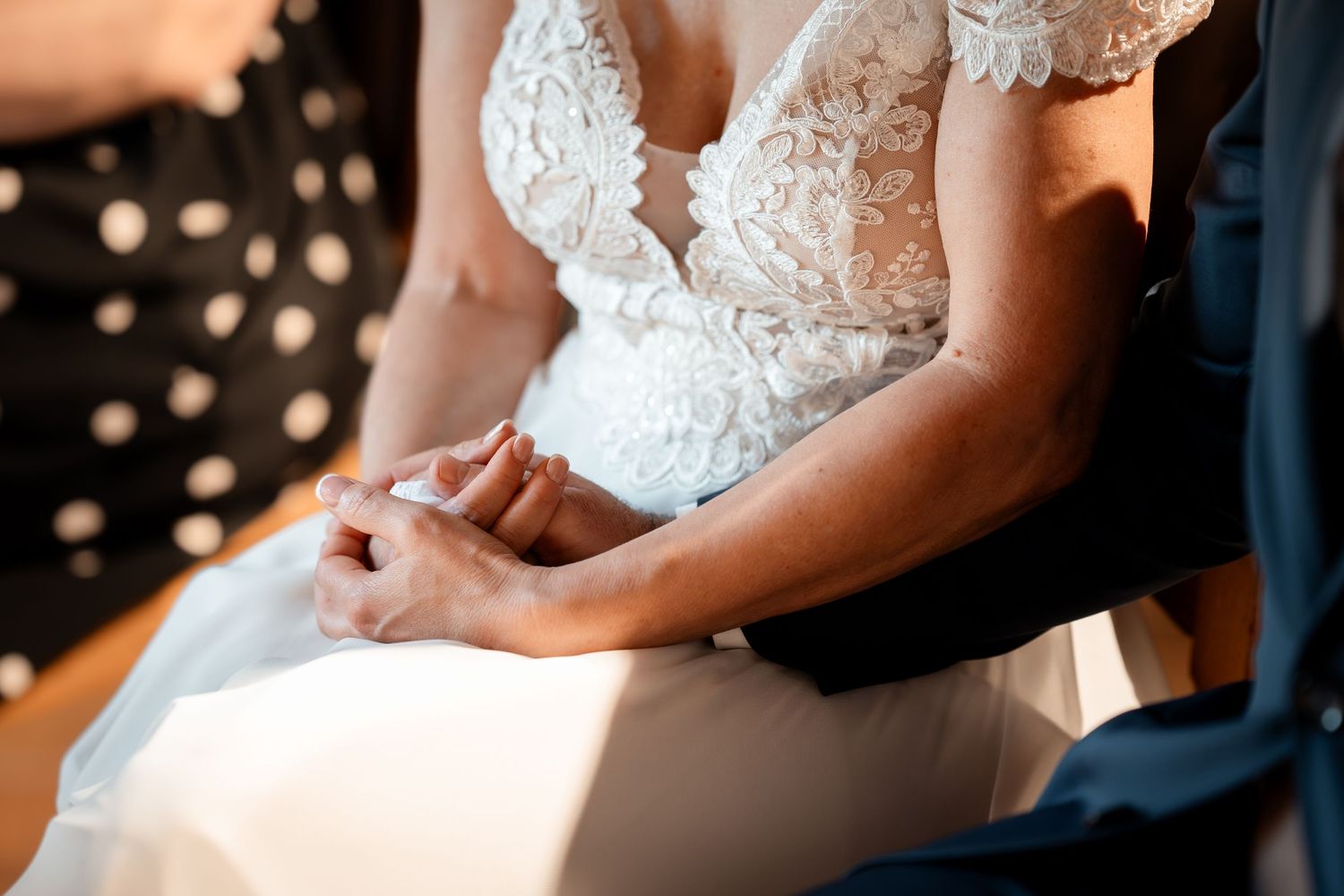 Close-up of bride and groom holding hands during wedding ceremony in lace bridal gown.