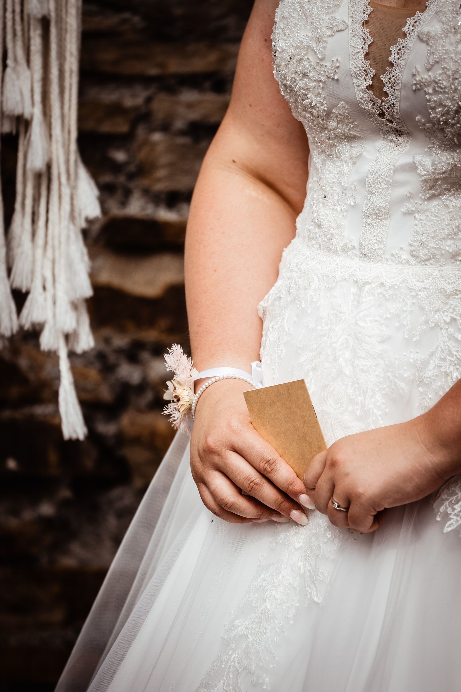 Bride in lace wedding dress holding vow card with floral wrist corsage.