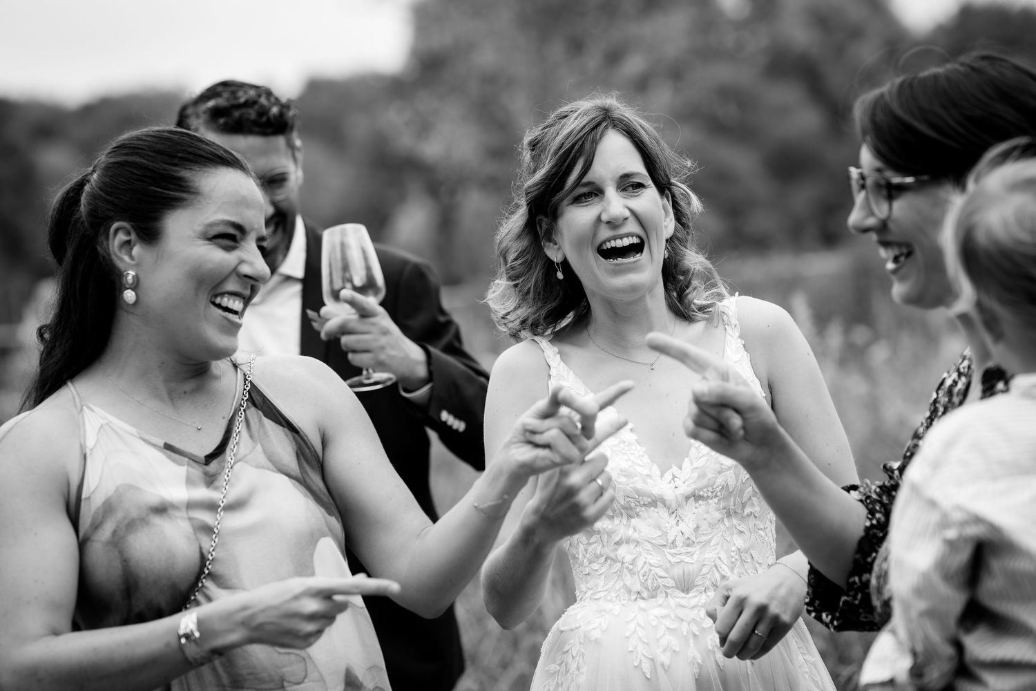 A laughing bride enjoys a joyful moment with wedding guests during an outdoor celebration.