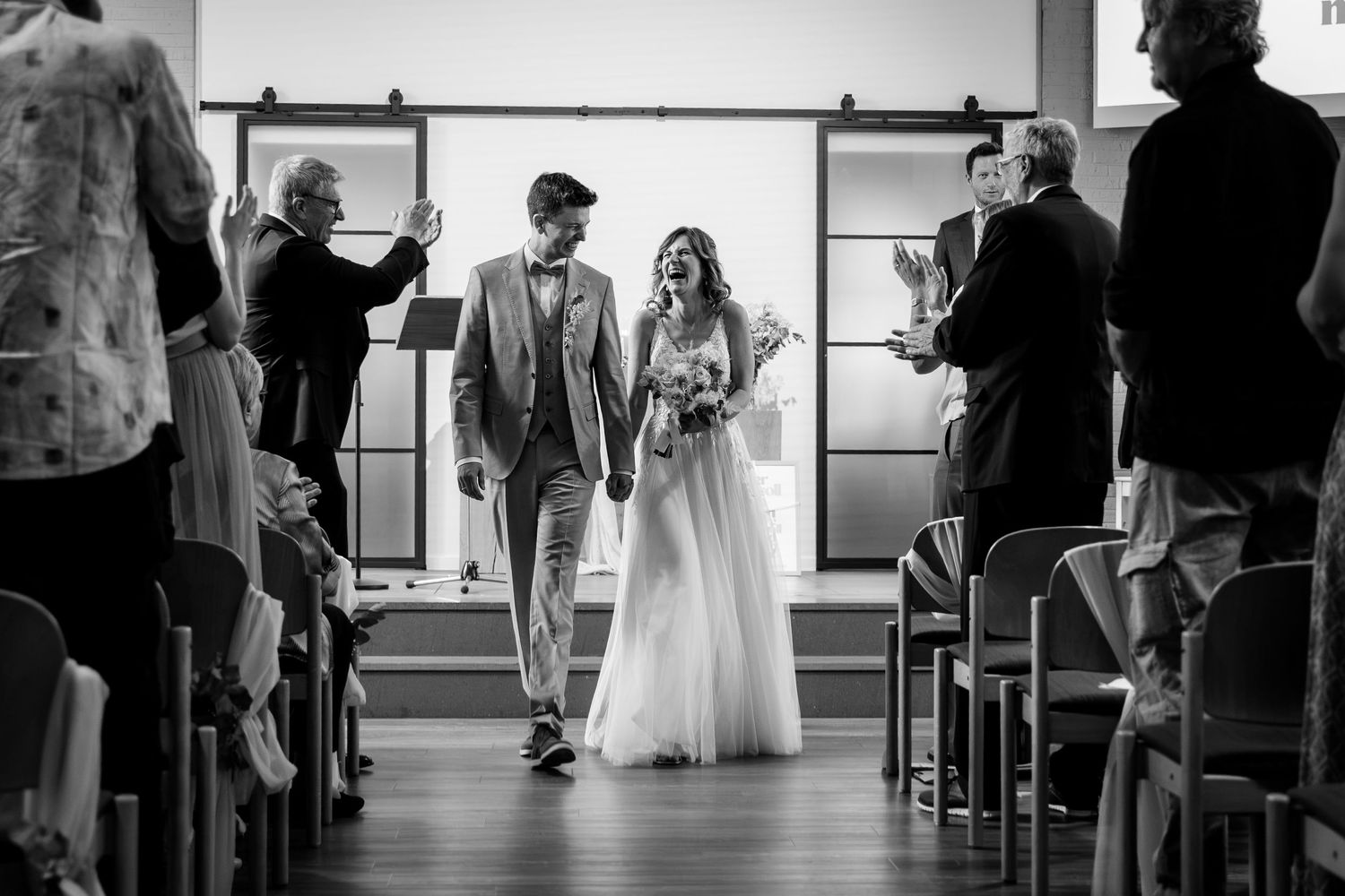 A bride and groom walk down the aisle together after their wedding ceremony in black and white.