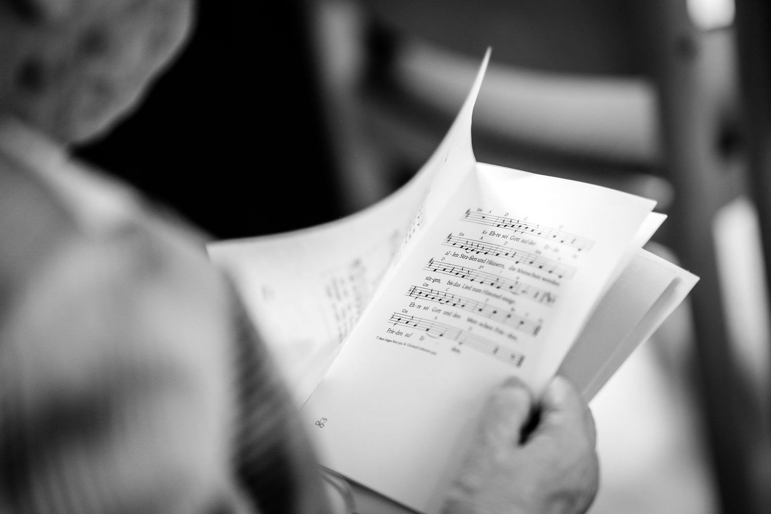 Person reading sheet music in black and white, holding printed musical score pages.