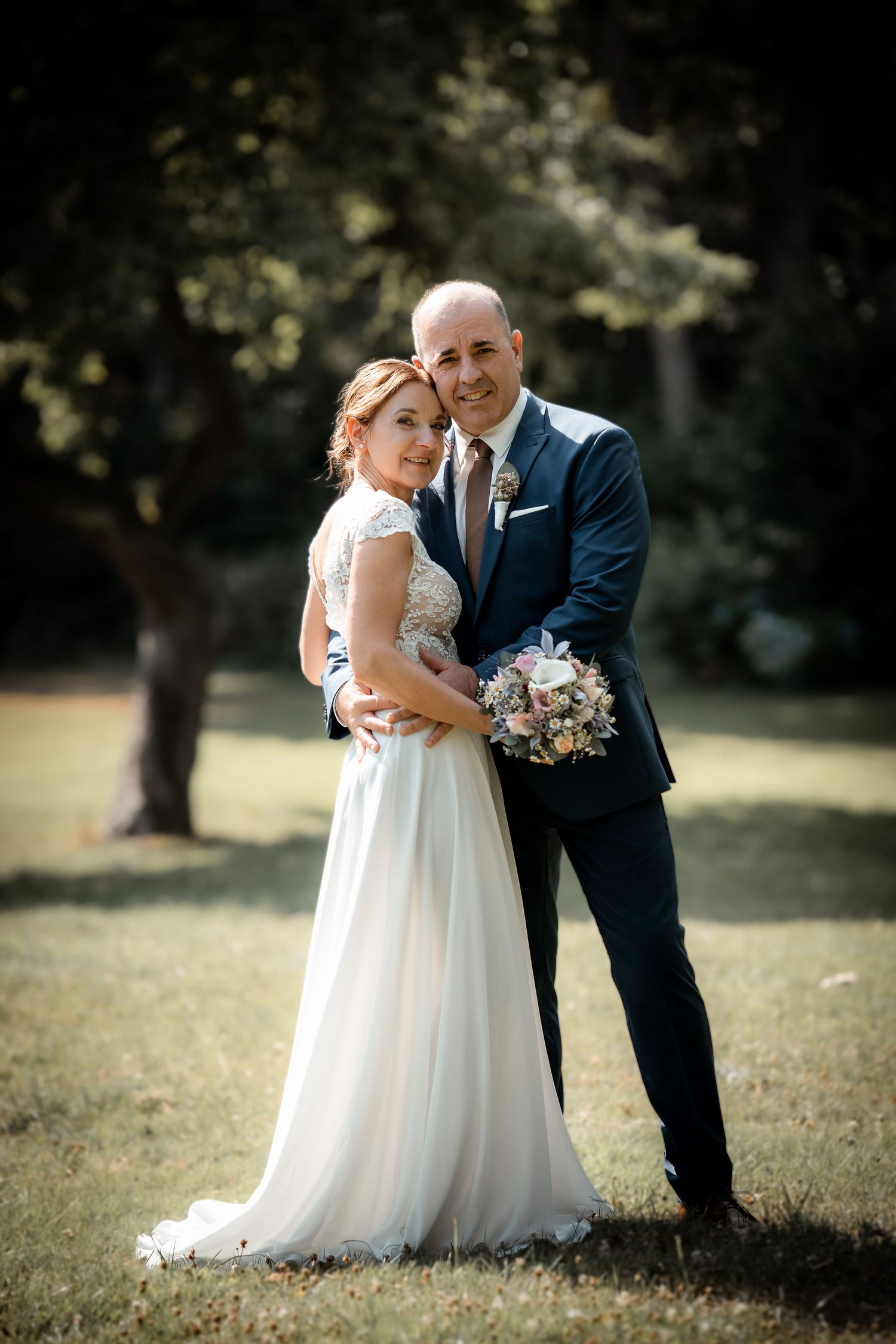 Bride and groom embrace in a sunlit garden, with the bride holding a pastel floral bouquet.