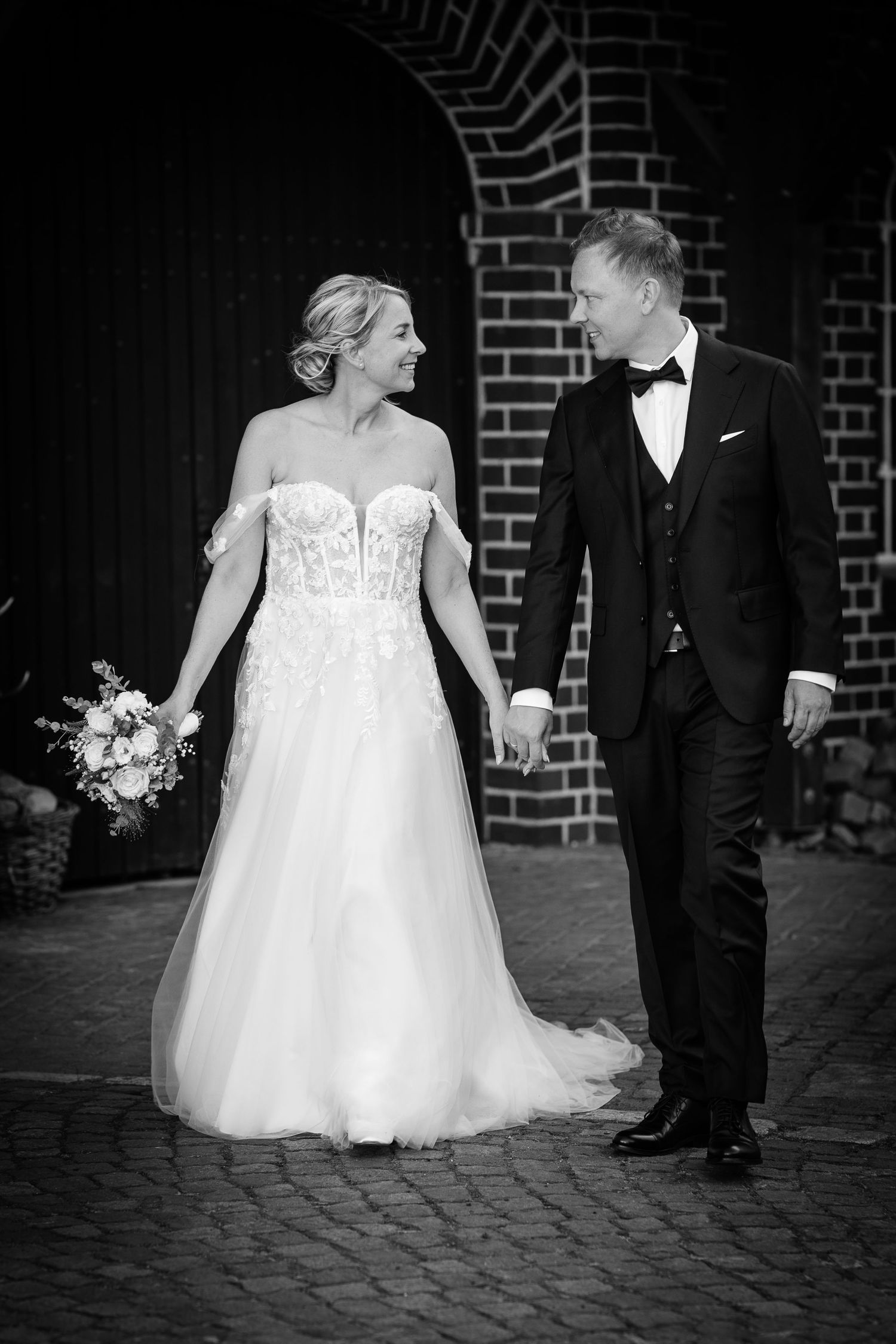 Bride and groom walking together smiling holding a bouquet in black and white wedding photo.