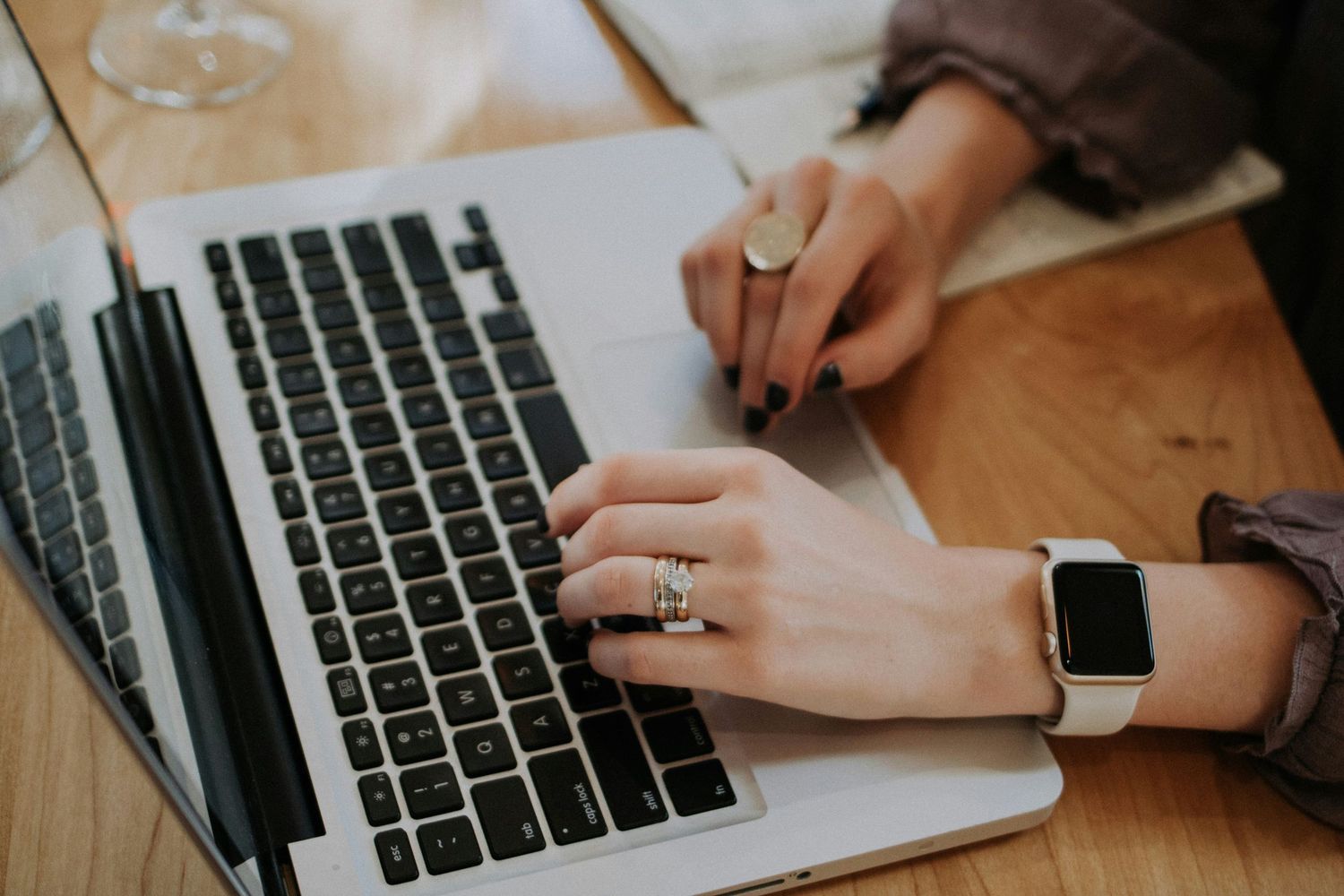 Hands typing on laptop keyboard while wearing smartwatch and ring.