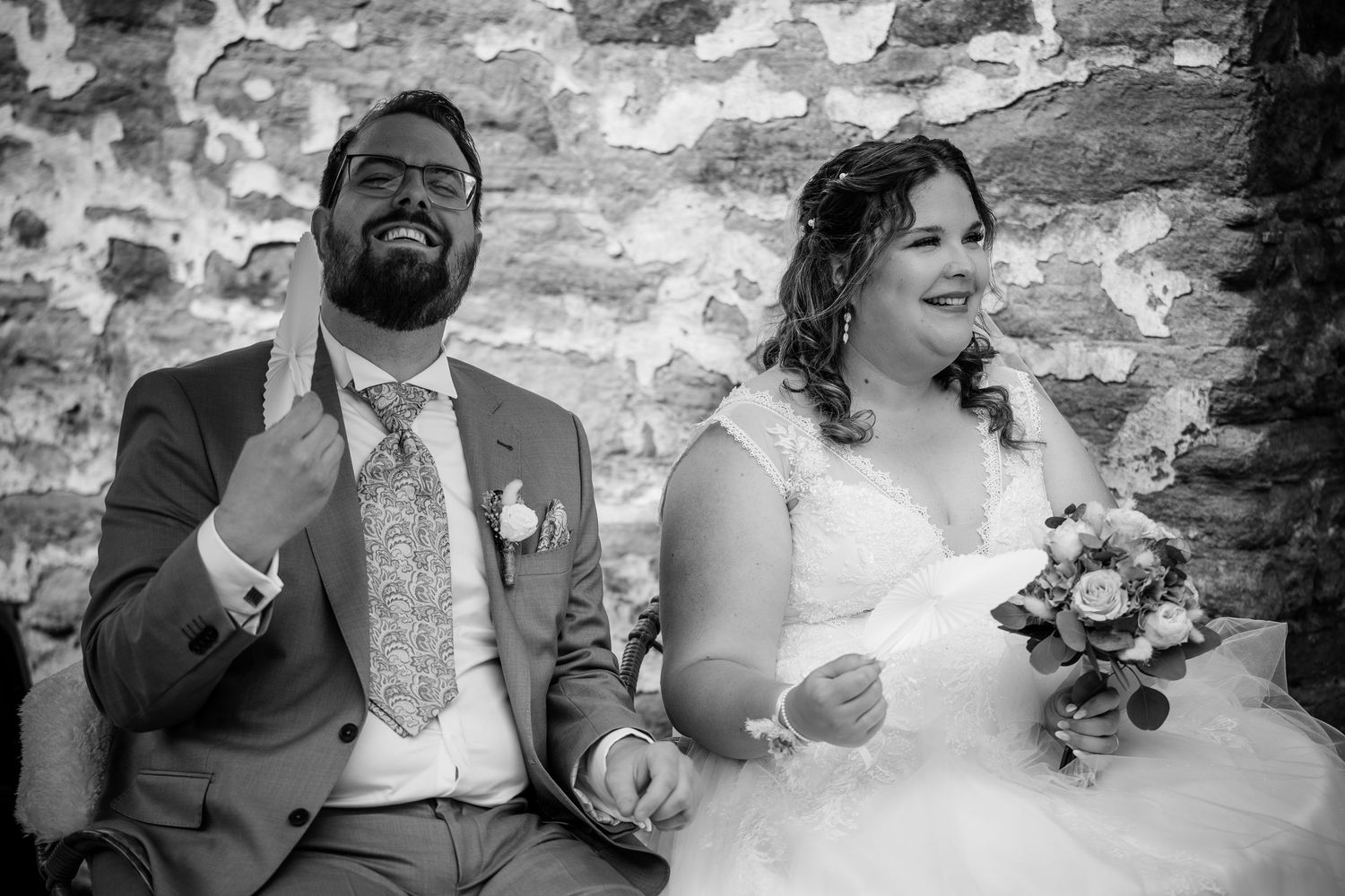 Black and white photo of laughing bride and groom sitting together during wedding ceremony.