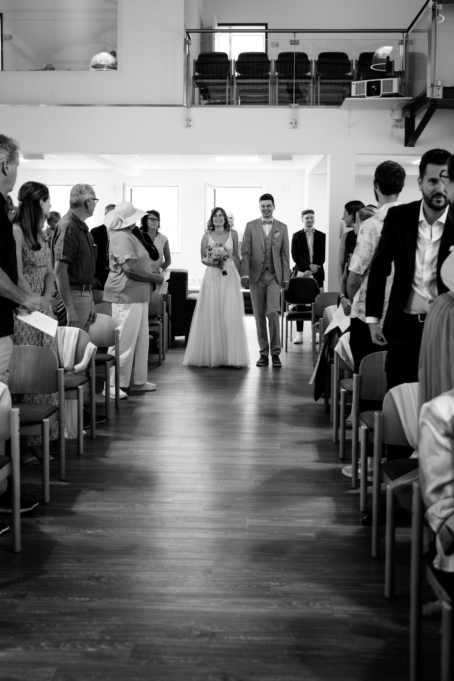 Black and white photo of a bride and groom walking down the aisle at an indoor wedding ceremony.