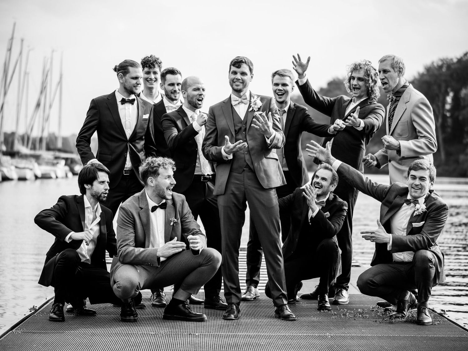 Wedding party members crouch down in a playful pose on a boardwalk for a fun group photo.