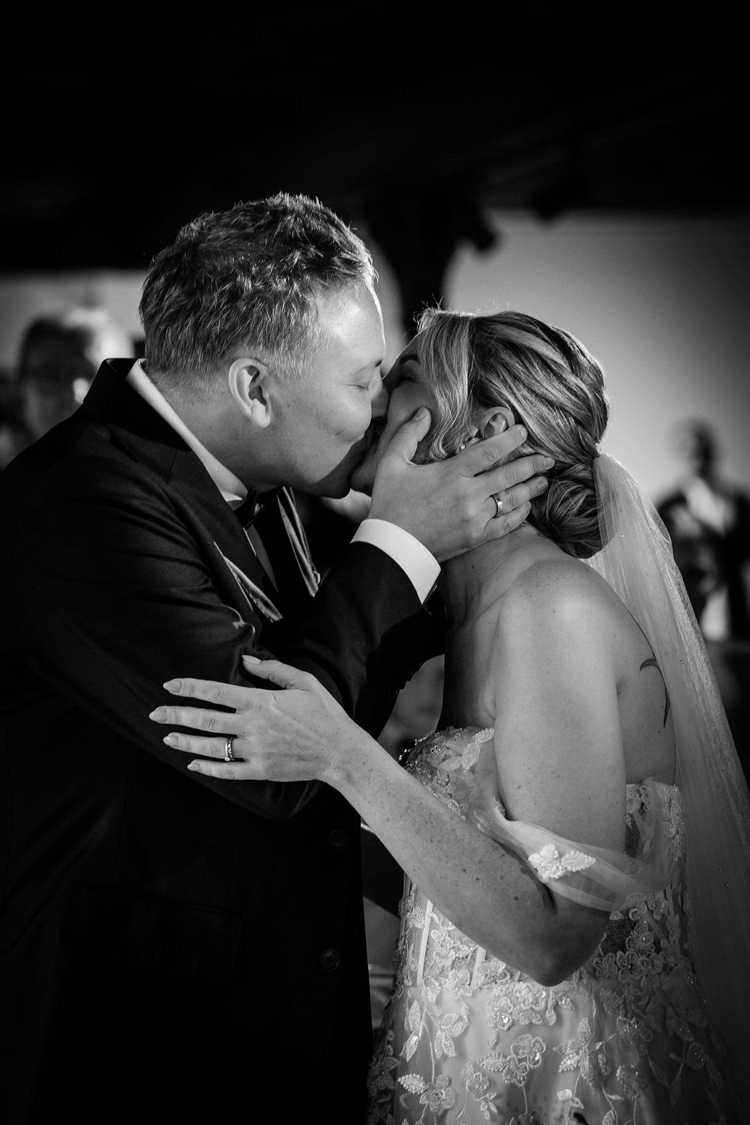 Black and white photo of a bride and groom sharing their first kiss at their wedding ceremony.