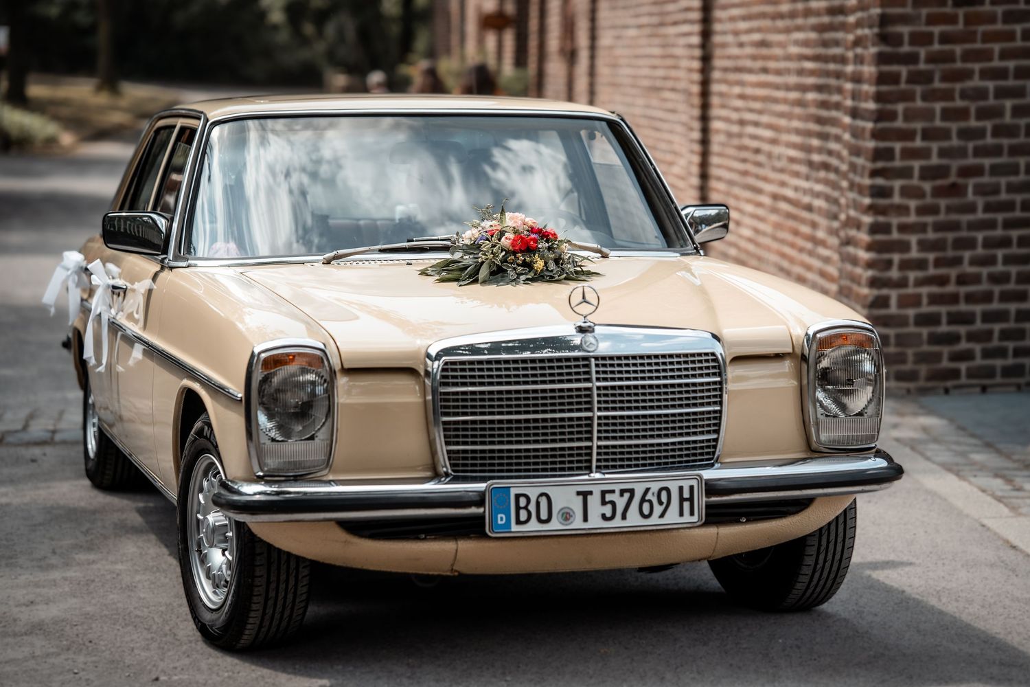 Vintage beige Mercedes-Benz wedding car decorated with floral arrangement on hood, Italian license plate BO T5769H.