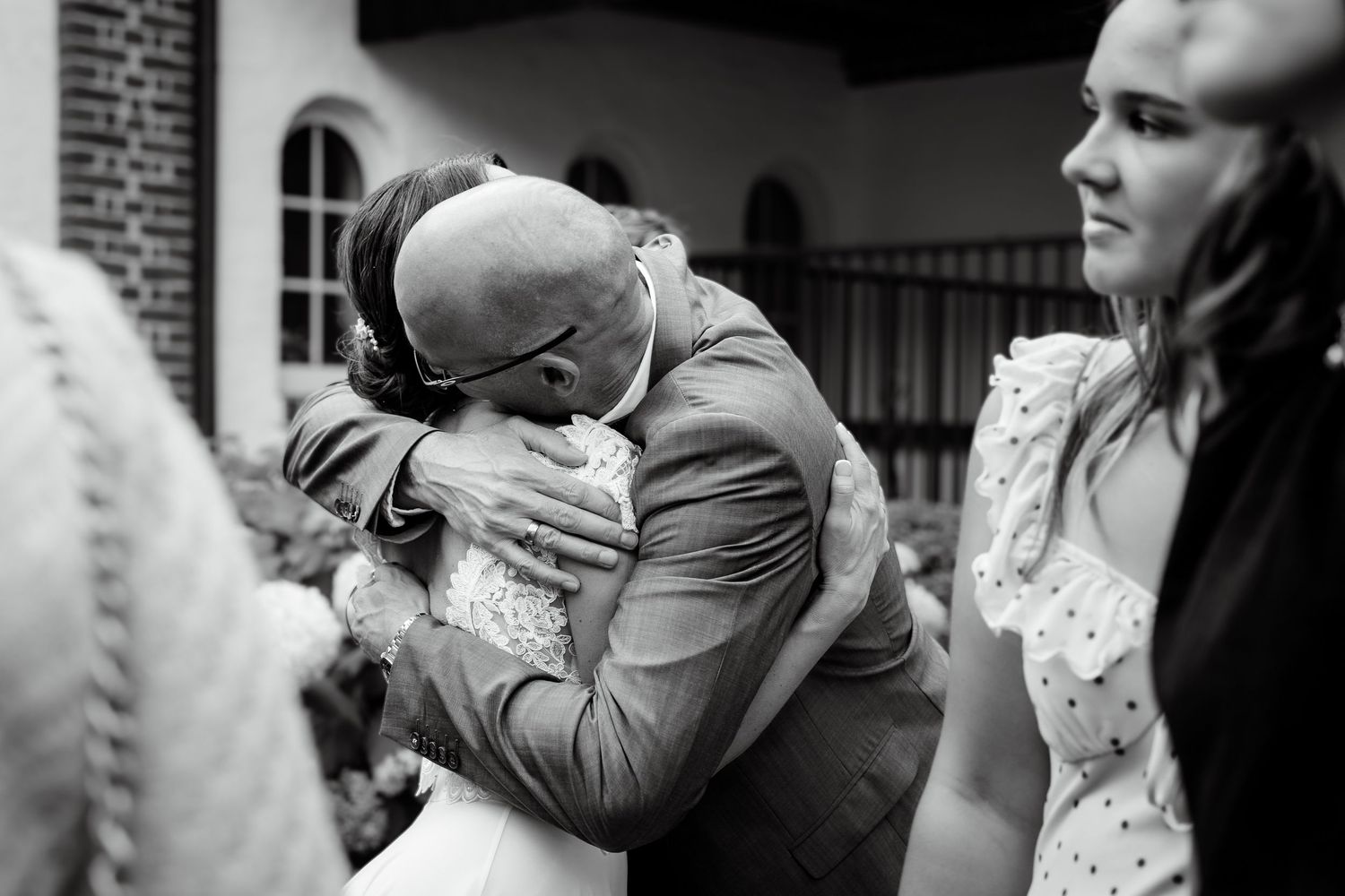 Emotional wedding hug between bride and guest in black and white photo outside a church.