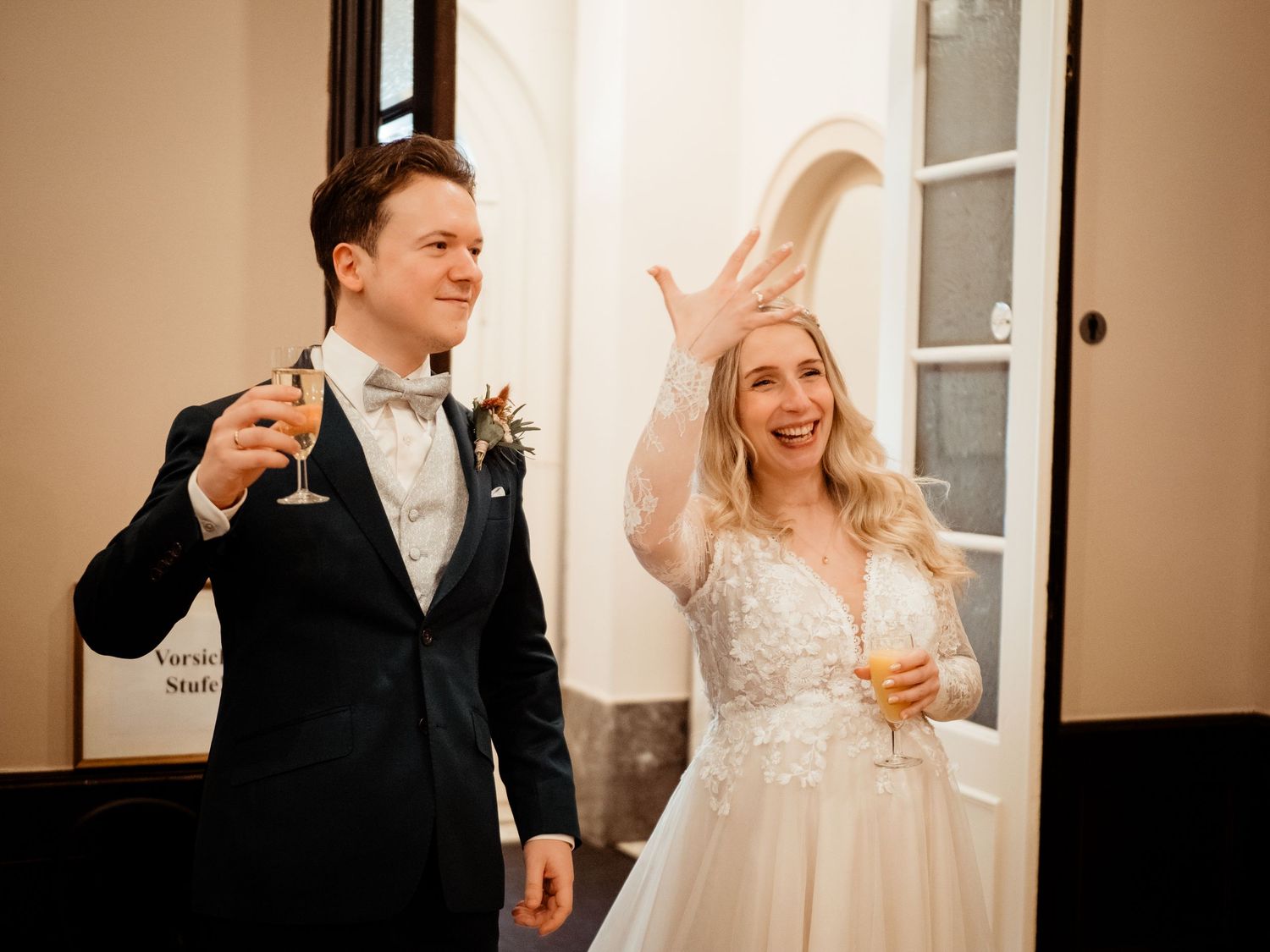 Bride and groom toasting with champagne glasses at their wedding reception, bride joyfully waving hand.