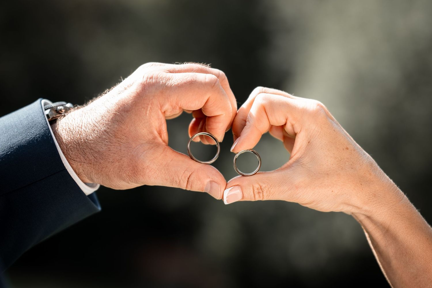 Bride and groom form a heart shape with their hands, each holding a wedding ring.