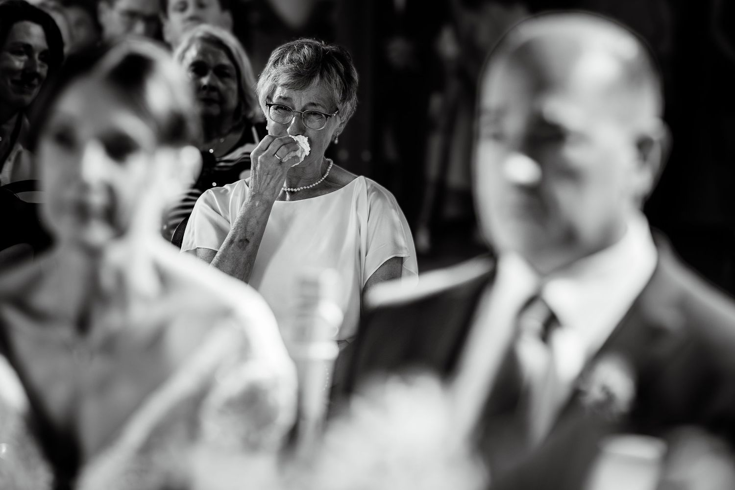 Emotional wedding guest wiping tears during ceremony in black and white crowd photo.