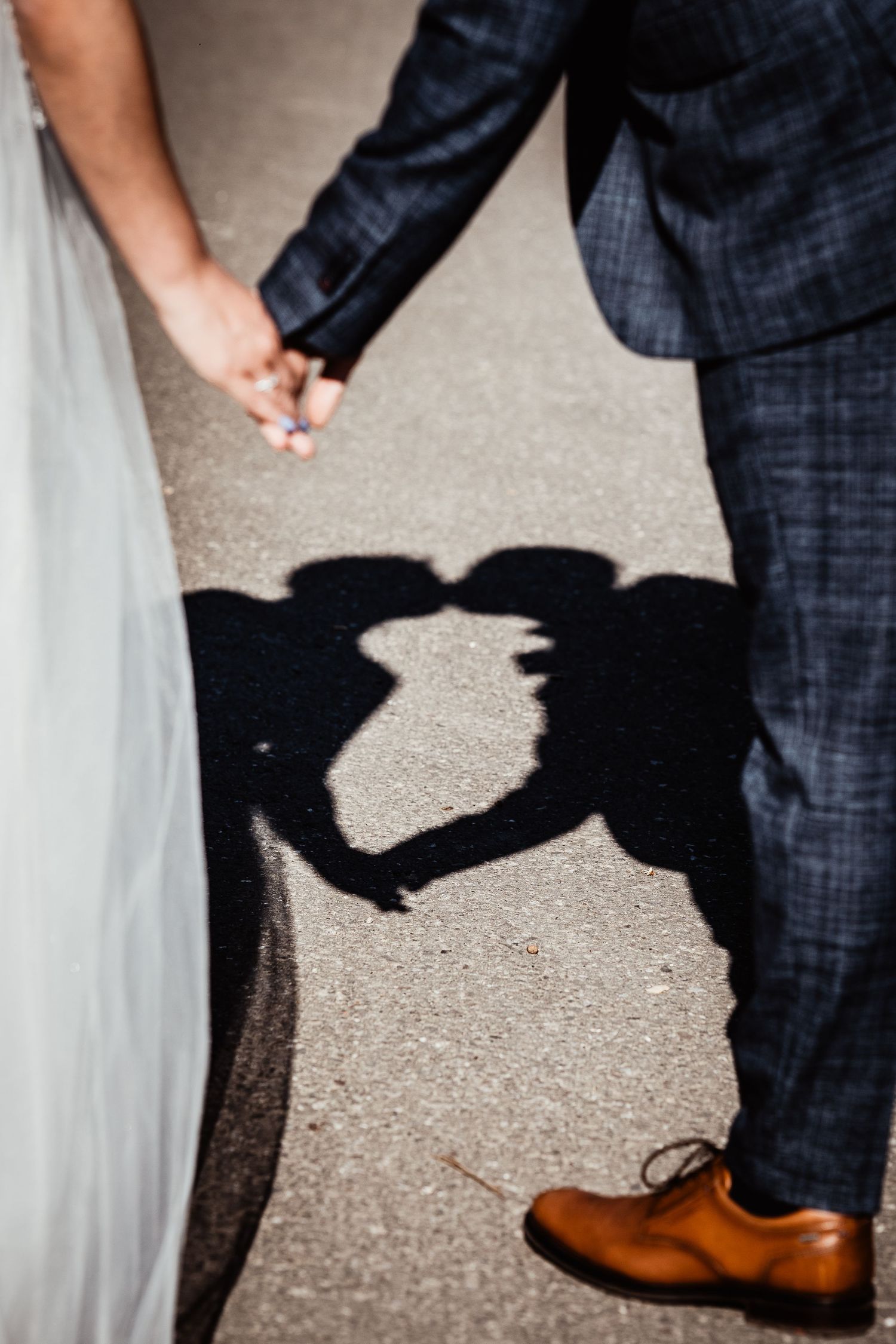 Wedding couple holding hands with romantic shadow silhouette kissing on pavement, groom in navy suit with brown shoes.