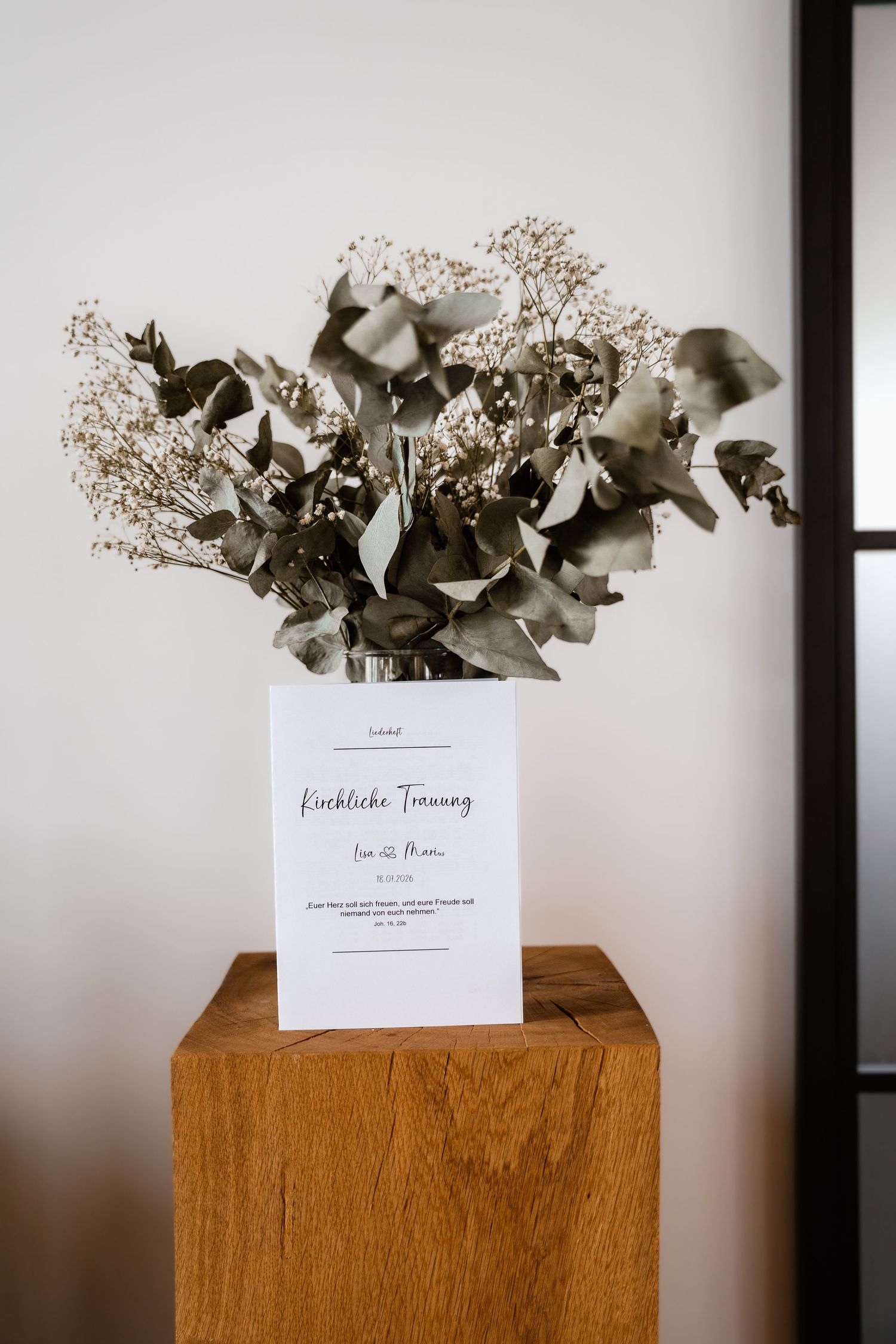 Elegant wedding ceremony sign for Kirchliche Trauung displayed on wooden pedestal with dried eucalyptus bouquet.
