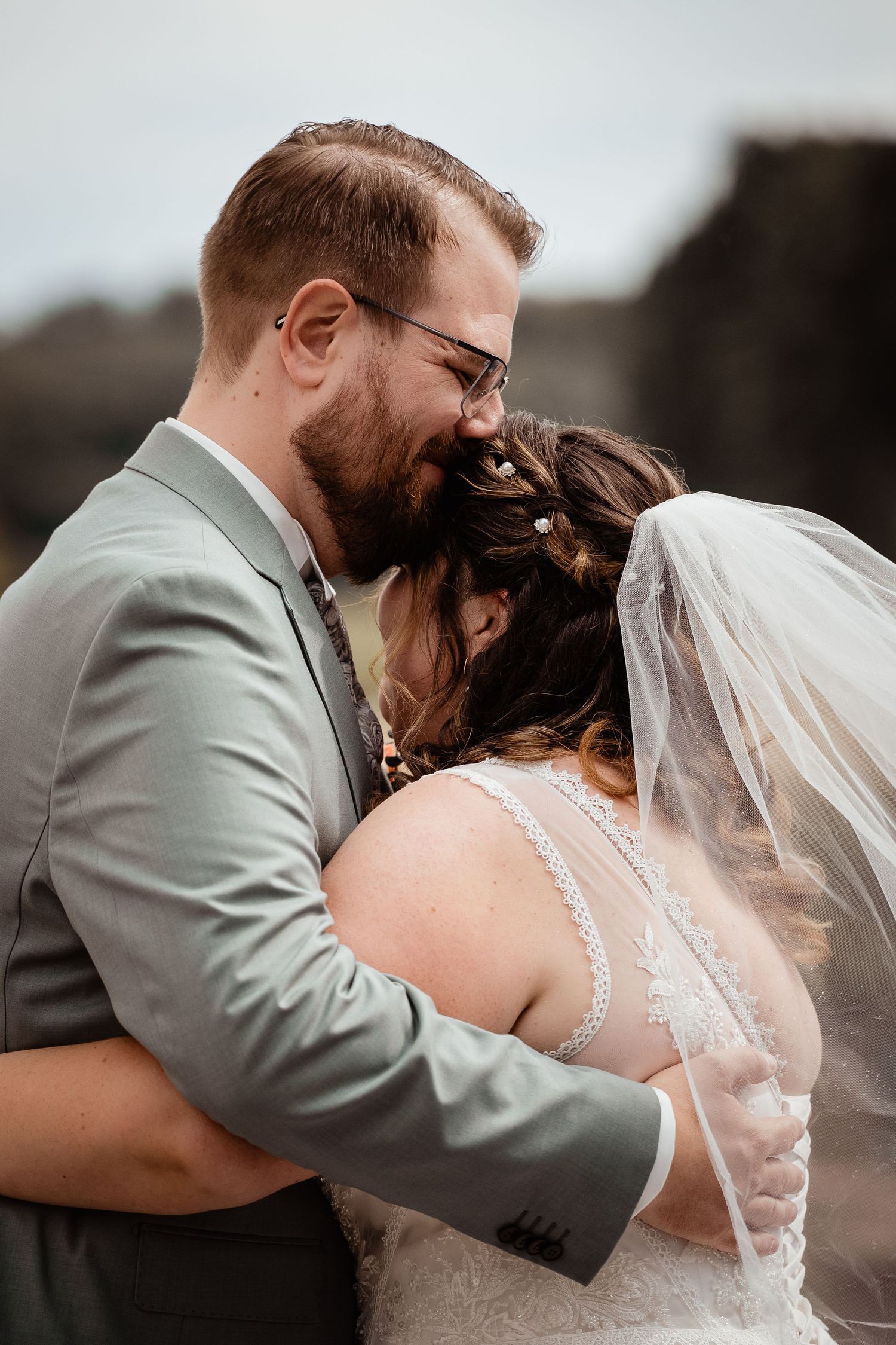 Bride and groom share an intimate kiss during their wedding ceremony, with her veil flowing in the breeze.
