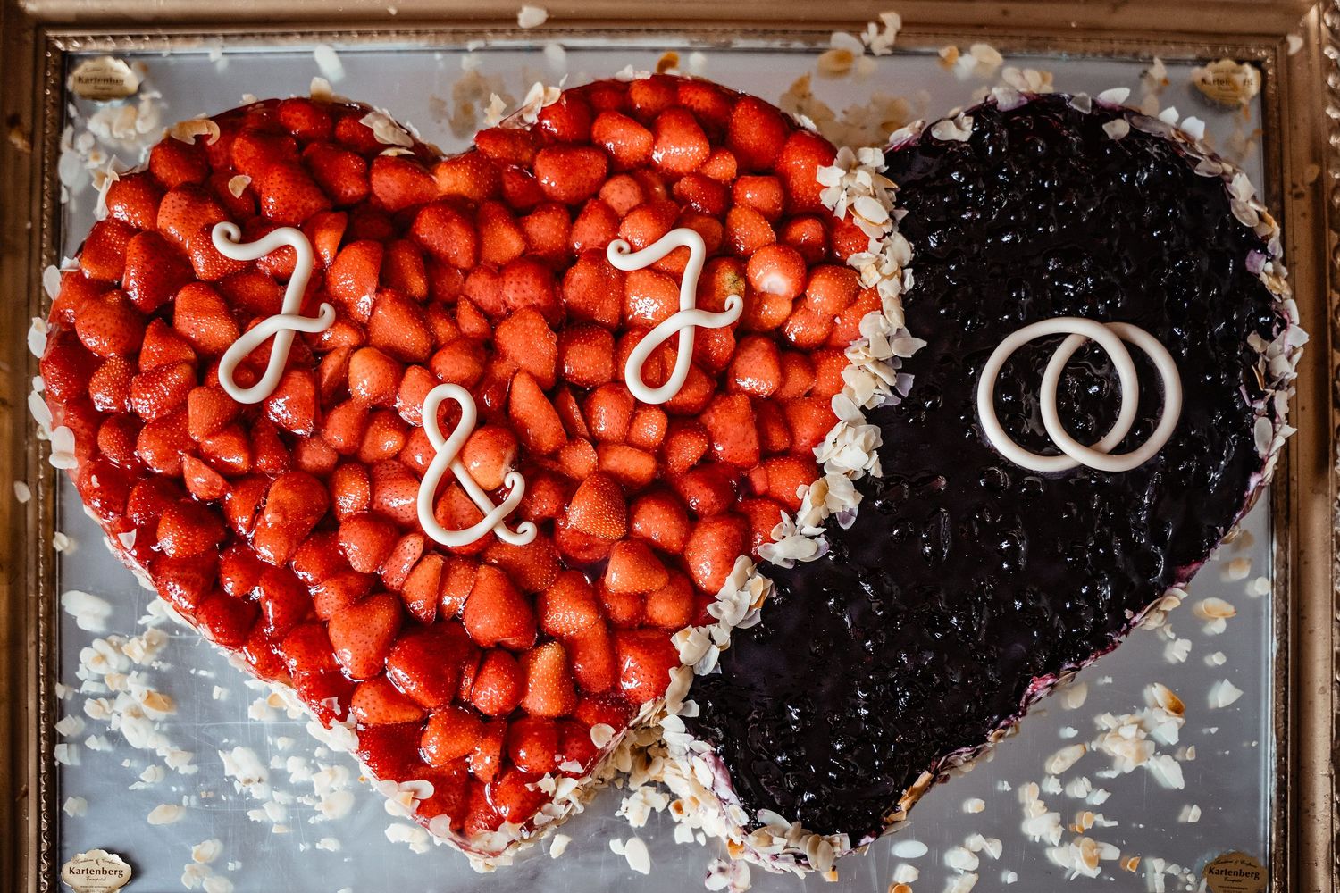 Heart-shaped wedding cake decorated with strawberries and blueberries with initials J and J.