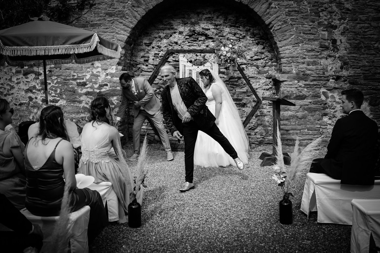 Black and white photo of bride and groom celebrating at outdoor wedding ceremony near stone arch.
