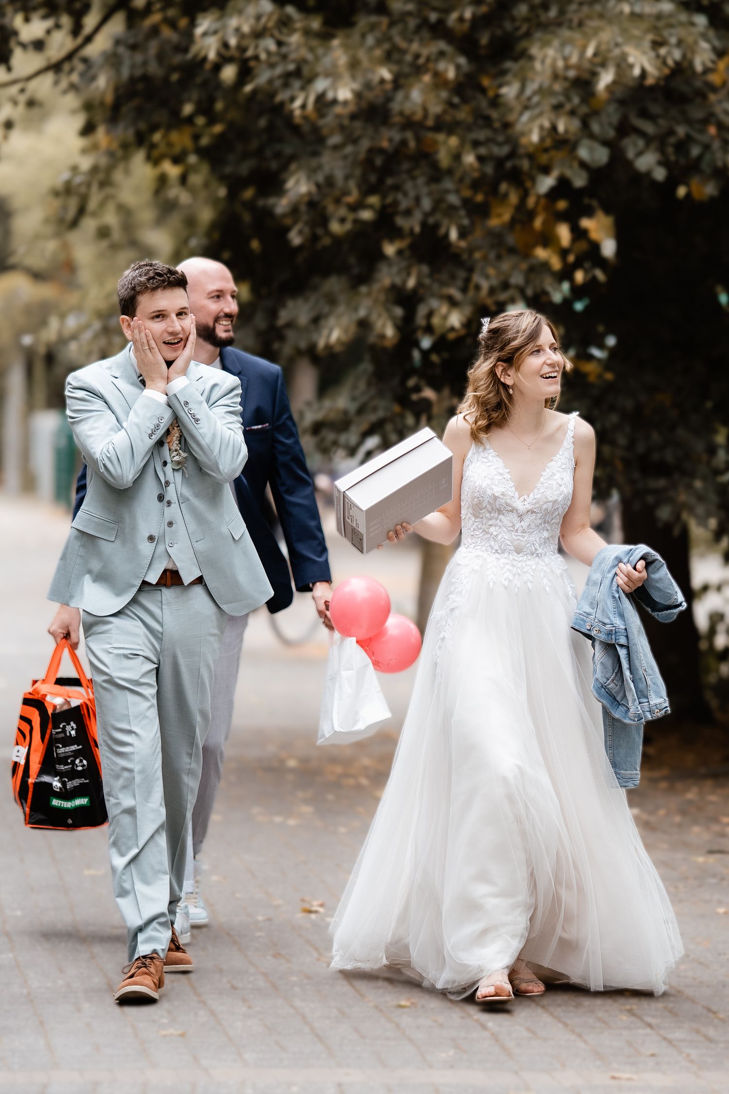 A joyful bride and groom walk outdoors carrying balloons and gifts on their wedding day.