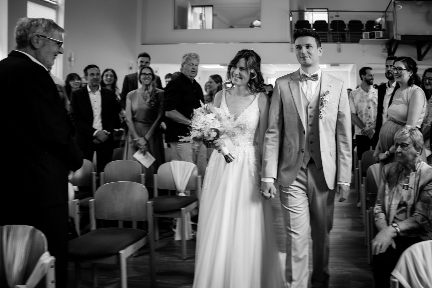 Bride and groom walk down the aisle hand in hand during wedding ceremony with guests seated nearby.