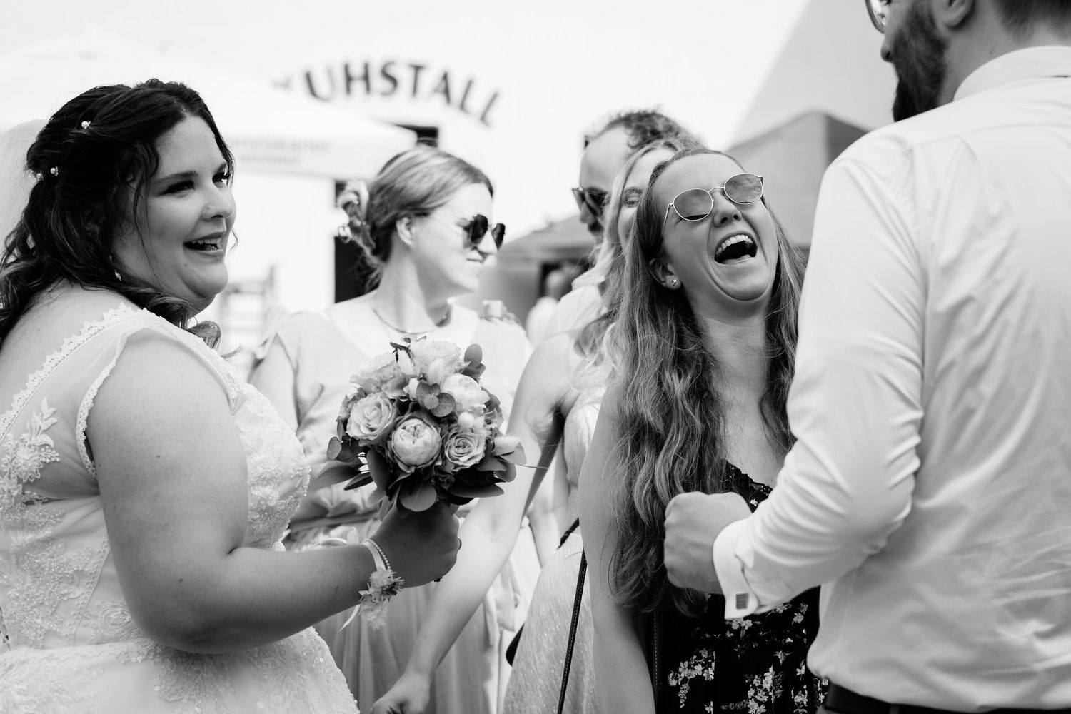 Black and white photo of joyful wedding guests laughing outside a venue after the ceremony.
