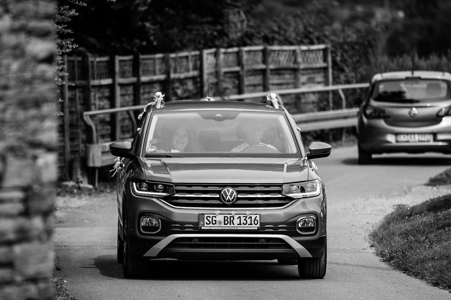 Black and white photo of a Volkswagen SUV driving on a narrow road through a lush green landscape.