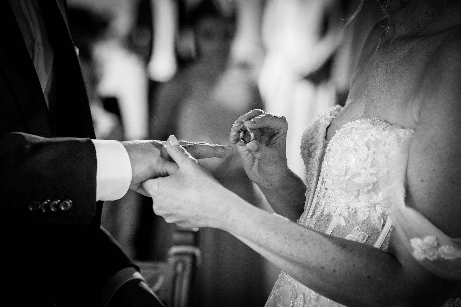Black and white photo of bride placing wedding ring on groom's finger during ceremony.