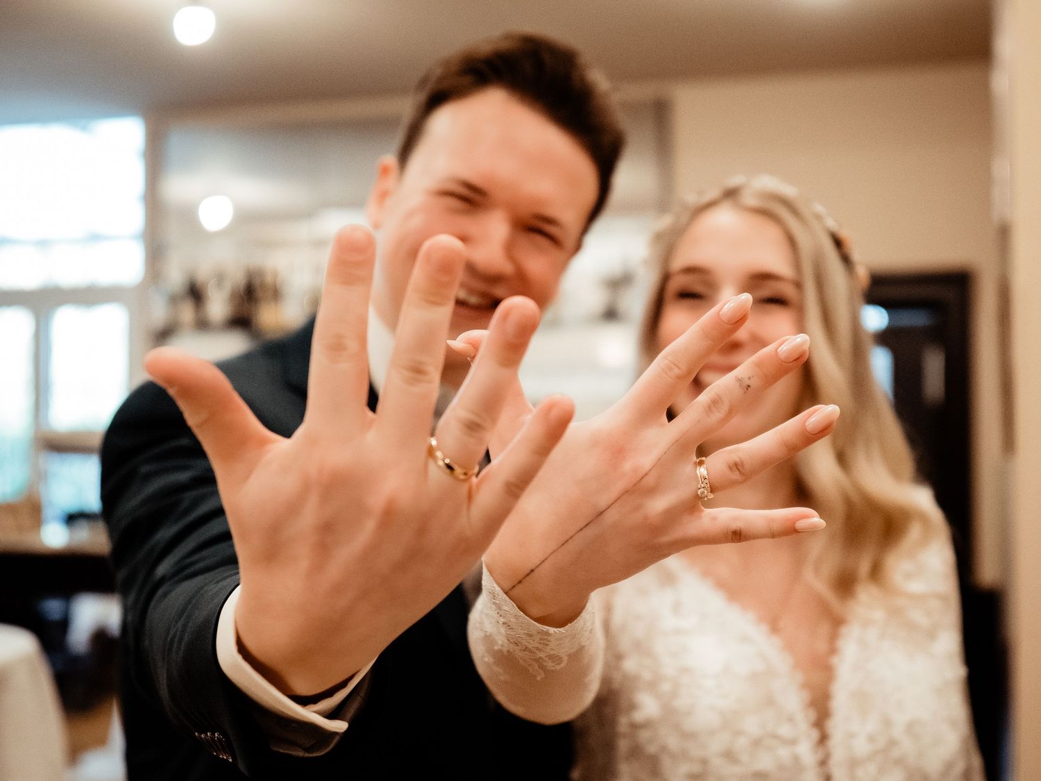 Smiling newlyweds showing off their wedding rings to the camera in a joyful close-up celebration photo.
