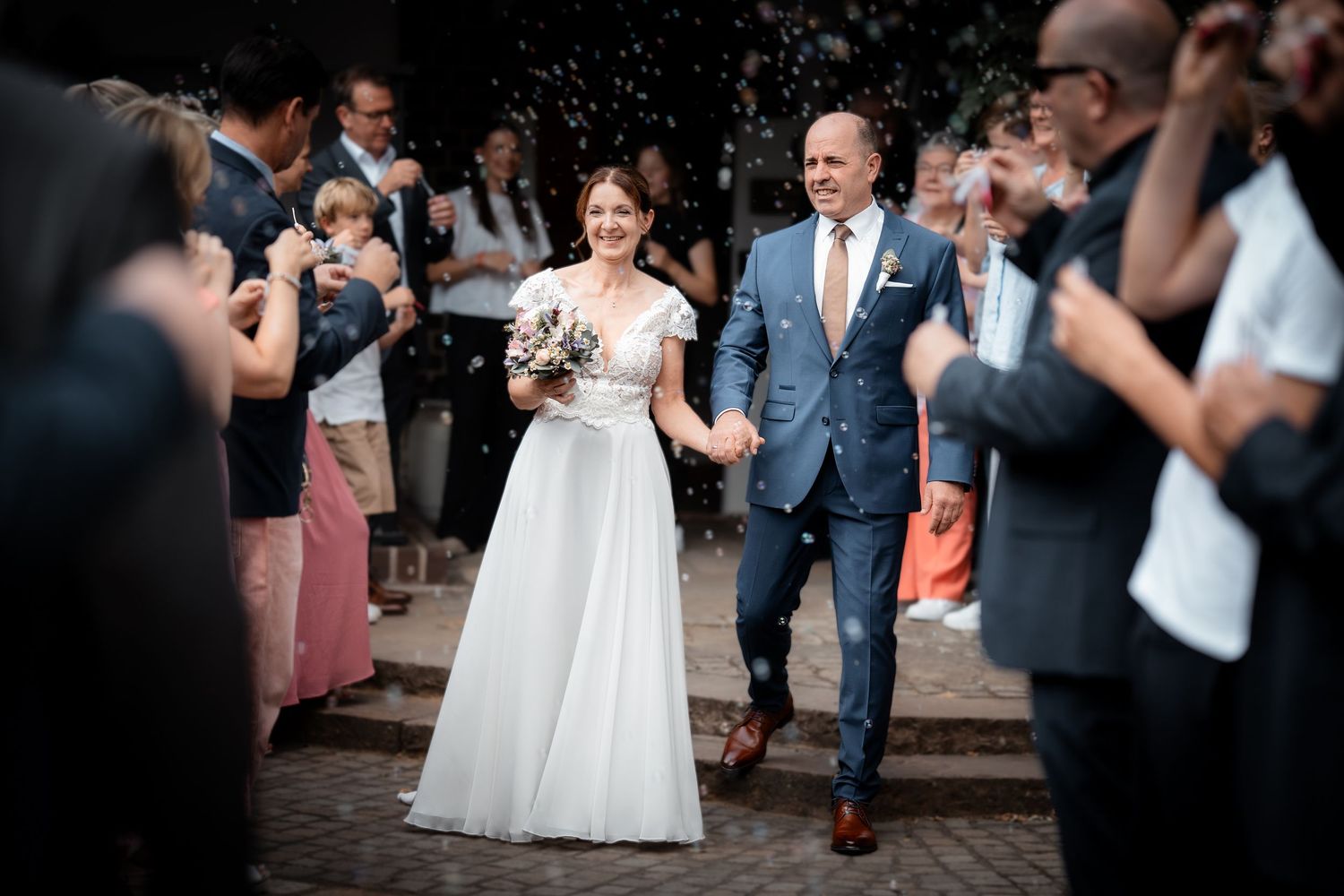 Newlyweds walk through confetti shower holding hands as wedding guests celebrate their ceremony exit.