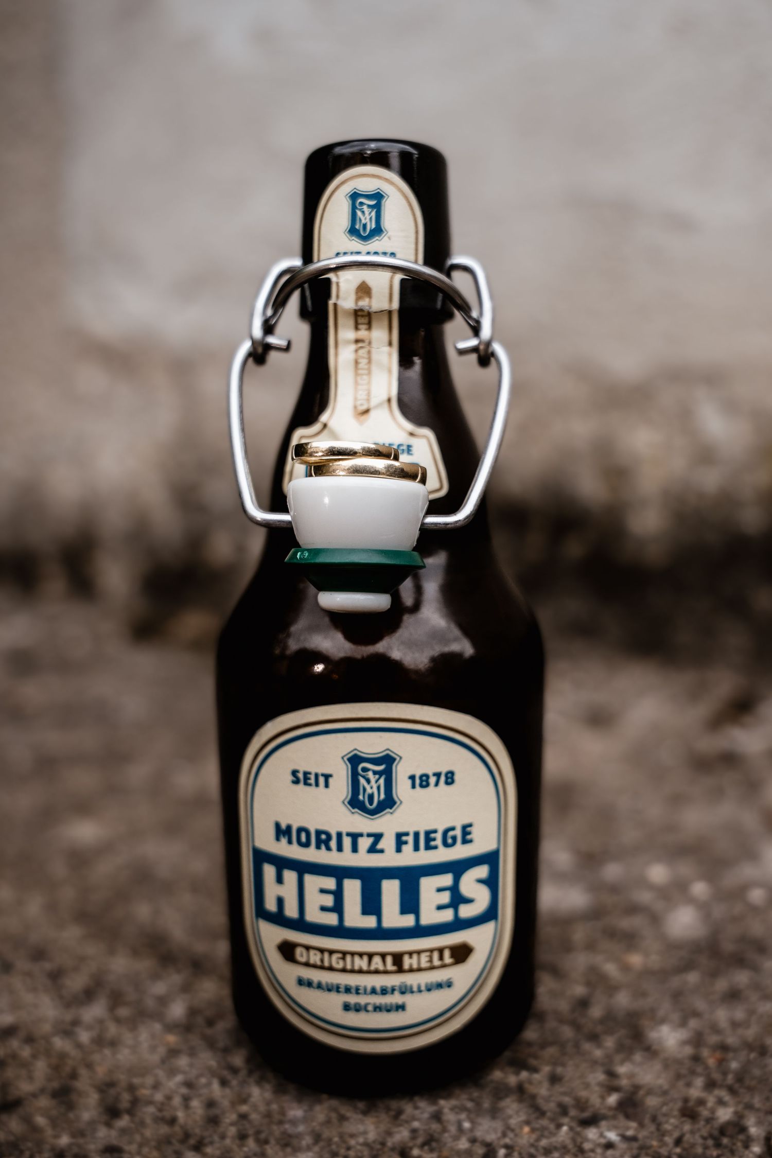 A close-up of a Moritz Fiege Helles beer bottle with a swing-top cap on a textured surface.