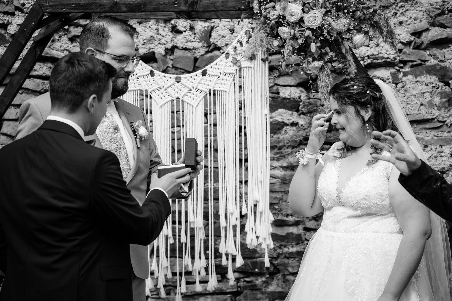 Emotional bride laughing during outdoor wedding ceremony with macrame backdrop and candles.