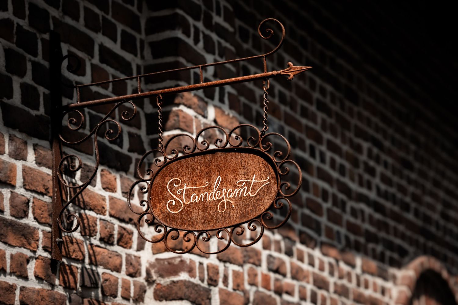Ornate rusty vintage oval sign reading Standpunt mounted on an old brick wall.