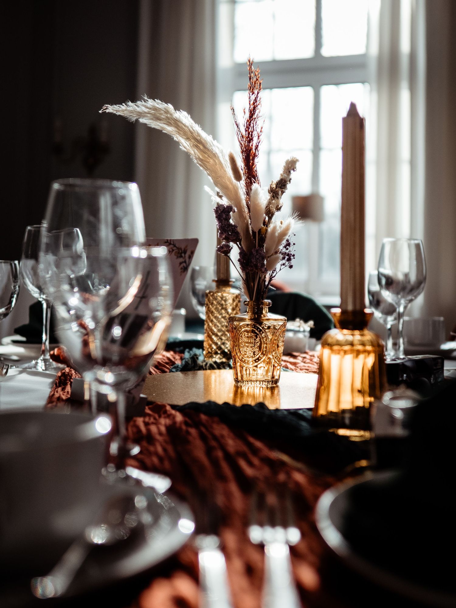 Elegant wedding table setting with amber glassware, dried floral centerpiece, and crystal wine glasses in warm candlelight.
