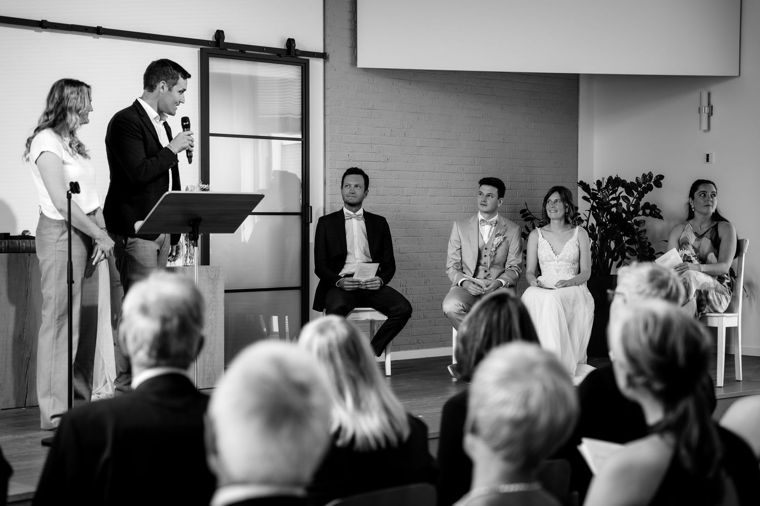 Black and white photo of wedding ceremony with officiant speaking at podium before seated guests.
