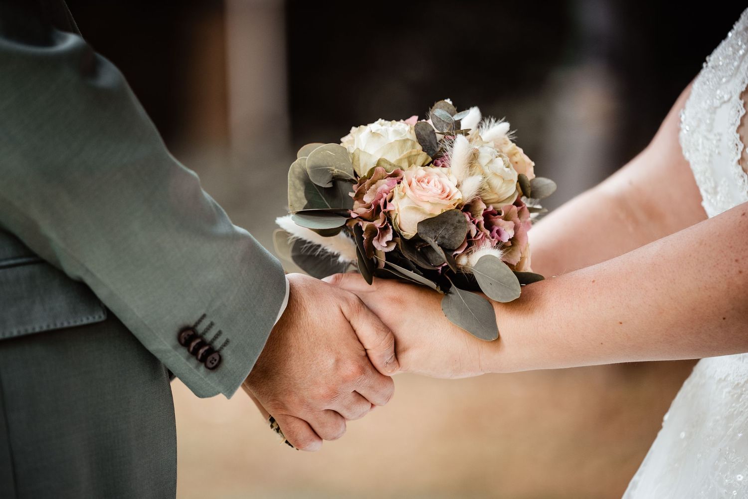 Bride and groom holding hands with a delicate bouquet of pink and white roses during wedding ceremony.