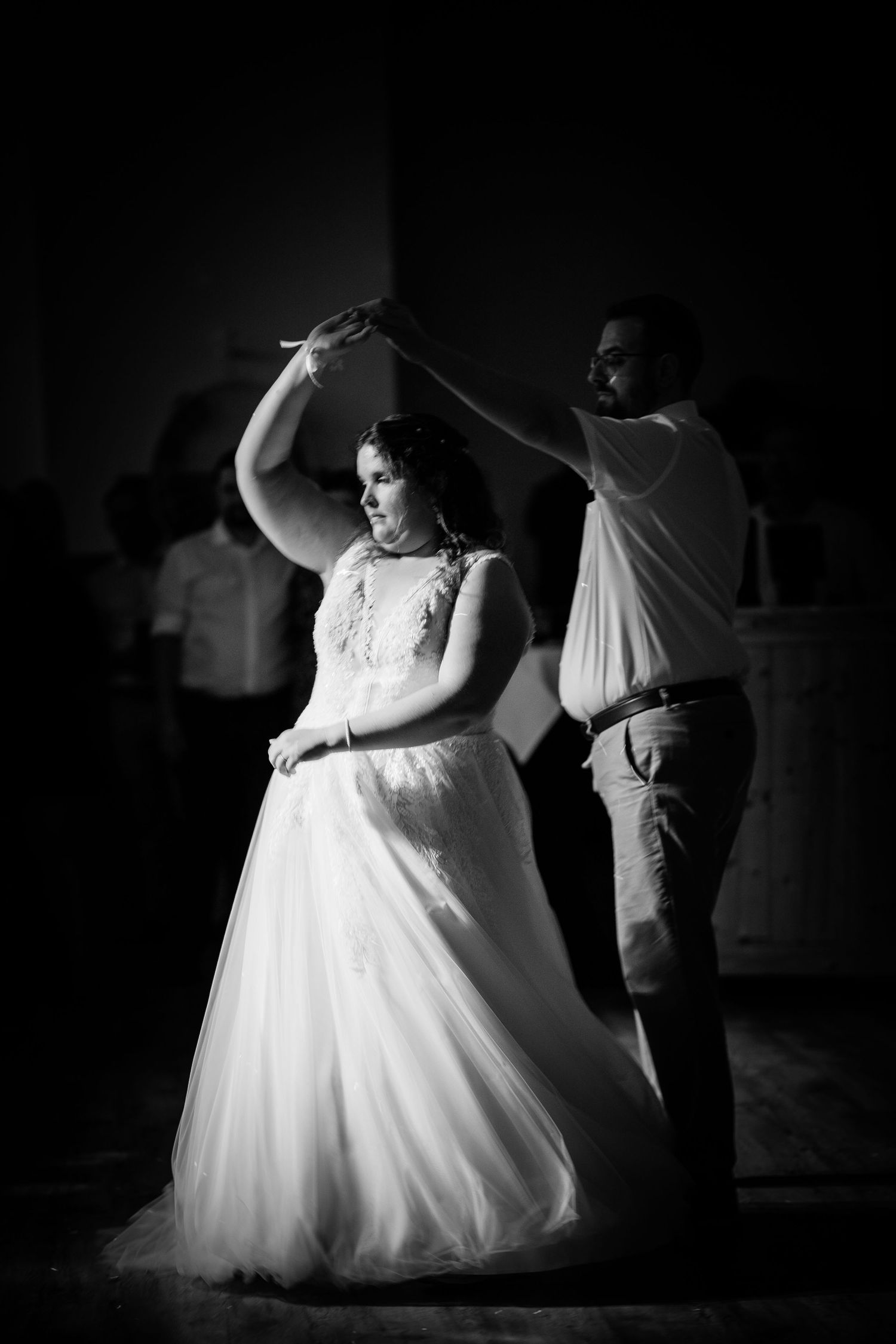 Bride and groom sharing elegant first dance with groom spinning bride in dramatic black and white photo.