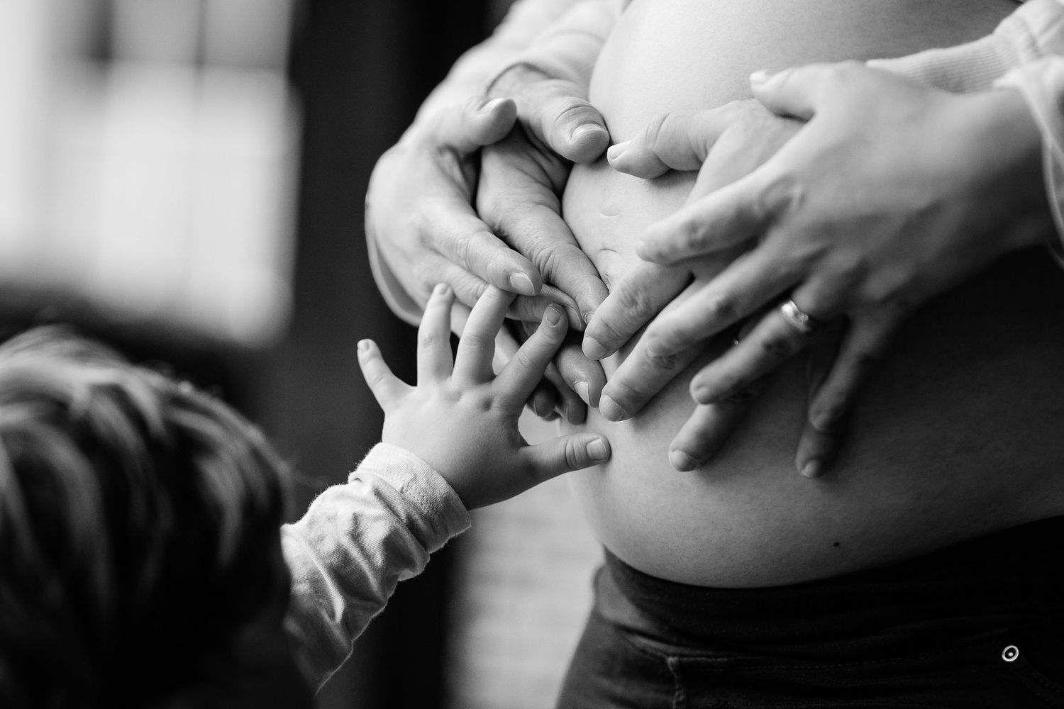 Black and white photo of family hands touching pregnant belly, maternity photography.