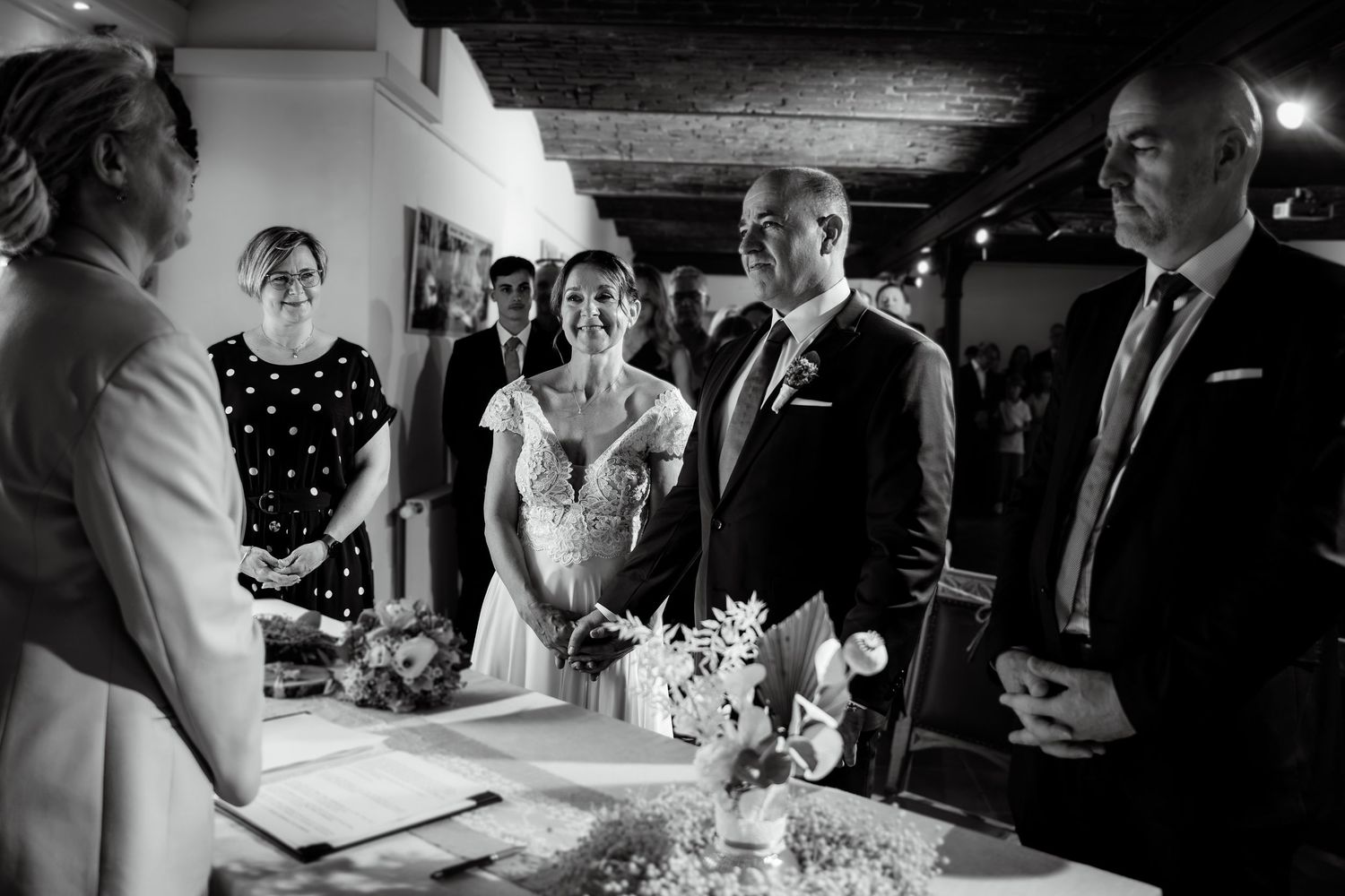 Black and white photo of a bride and groom exchanging vows at an elegant indoor wedding ceremony.