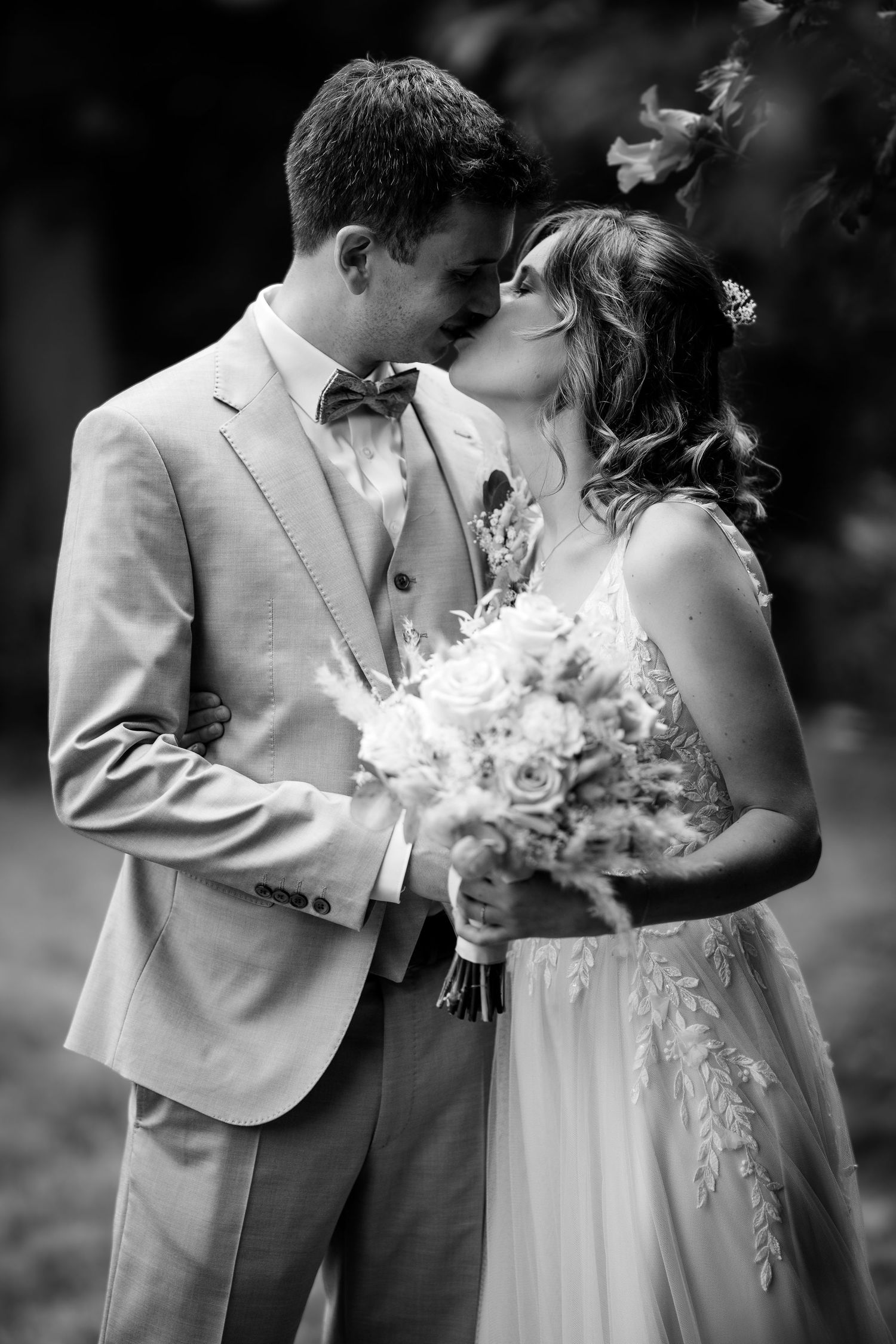 Black and white photo of a bride and groom sharing a tender kiss, bride holding a bouquet of roses.