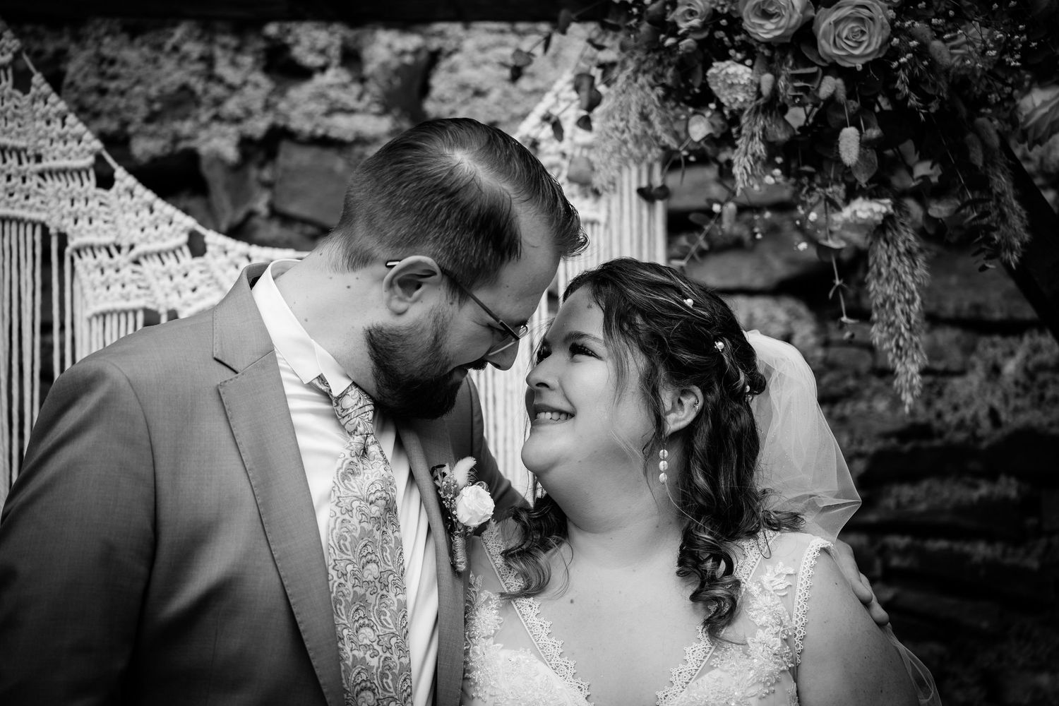 Black and white photo of a bride and groom sharing an intimate moment, touching foreheads and smiling at their wedding.