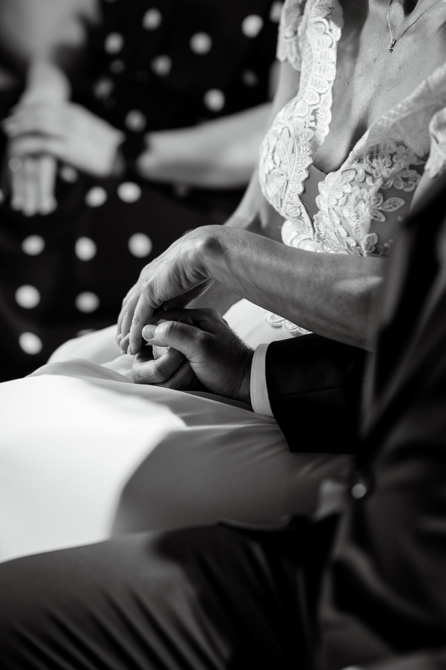 Black and white close-up of bride and groom holding hands tenderly during wedding ceremony.
