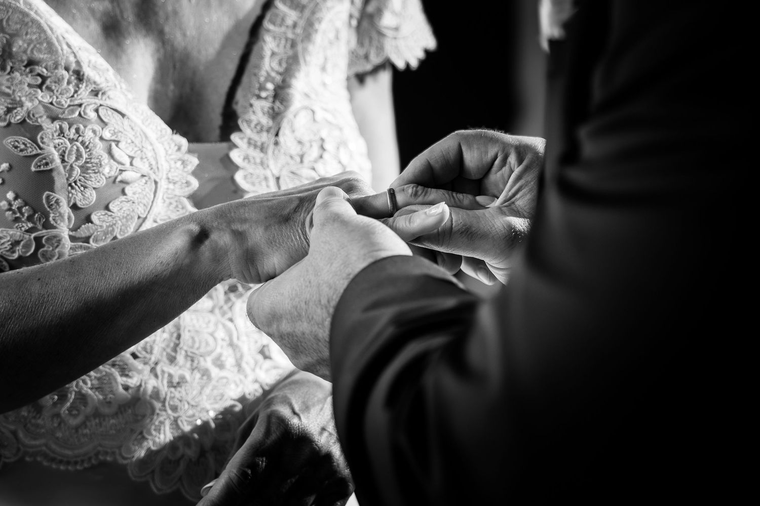 Black and white photo of a bride and groom exchanging wedding rings during their ceremony.